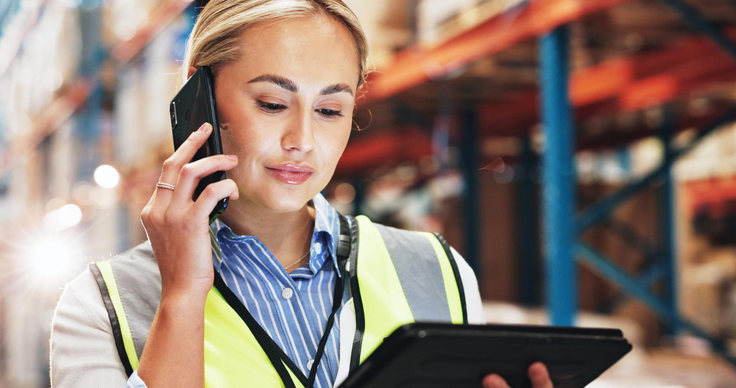 Szállítási információk témájú kép, amelyen egy raktári munkatárs telefonon egyeztet és tableten ellenőrzi a rendeléseket.